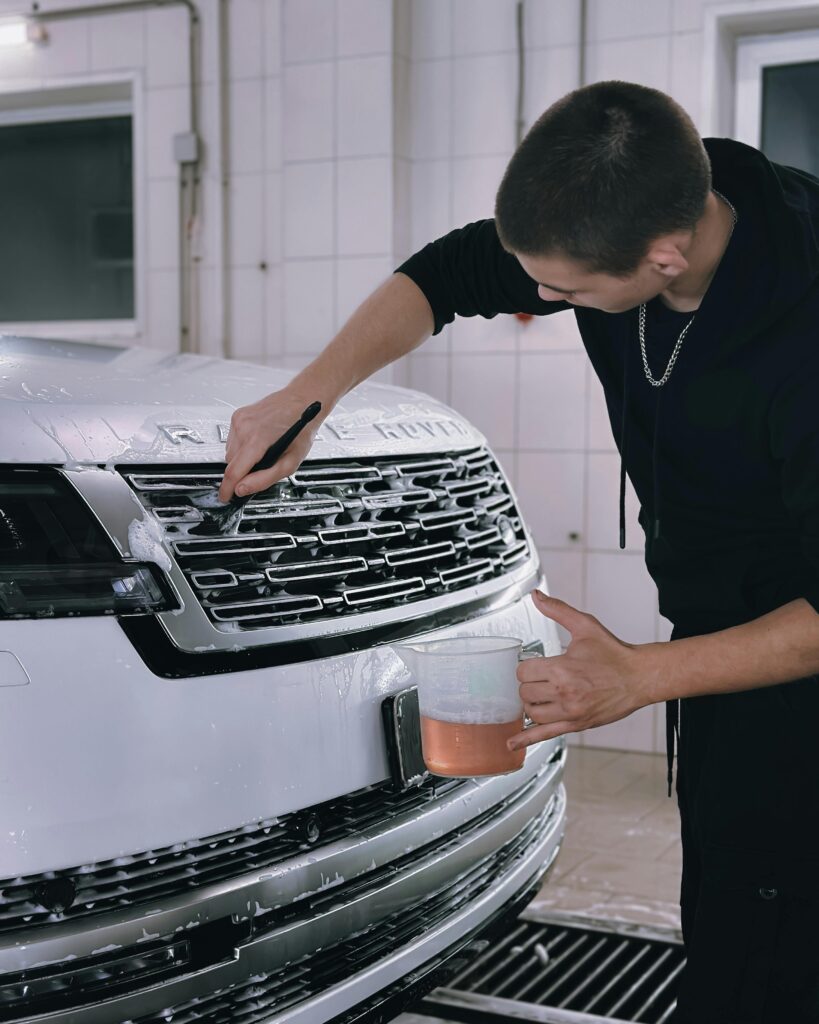 pexels-photo-30589155-30589155 A man washing a white luxury vehicle's grill in an indoor garage, focusing on cleanliness.